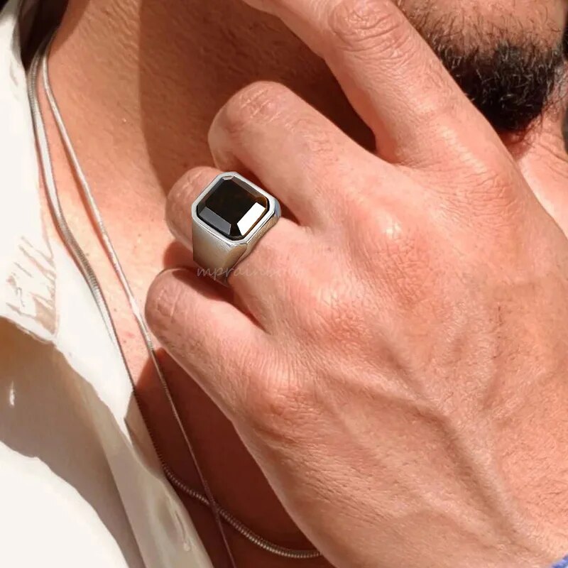 Anel masculino quadrado com pedra preta lapidada em aço, sendo usado no dedo para mostrar o ajuste e o impacto visual da peça.