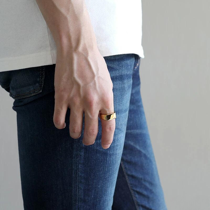 Anel masculino Flat Clássico em aço inoxidável dourado sendo usado com uma camisa branca e calça jeans, destacando seu visual casual