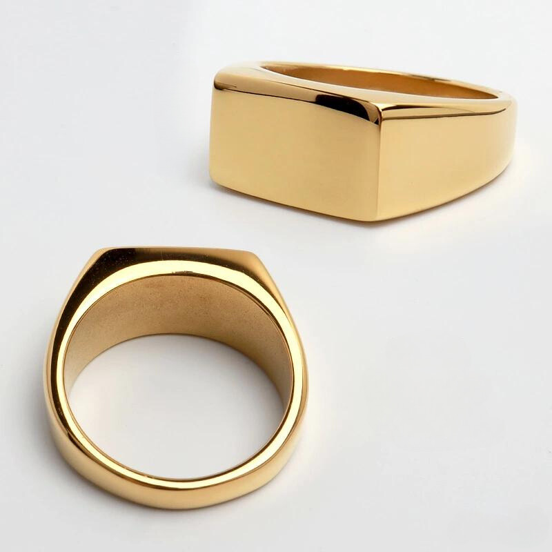 Dois anéis masculinos Flat Clássico em aço inoxidável dourado exibidos em diferentes ângulos com fundo claro.