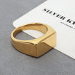 Anel masculino Flat Clássico em aço inoxidável dourado com fundo cinza e branco, em um ângulo que mostra seu acabamento polido.