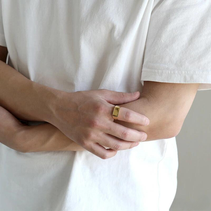 Anel masculino Flat Clássico em aço inoxidável dourado sendo usado com os braços cruzados e camisa branca, destacando seu estilo formal.