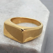 Anel masculino Flat Clássico em aço inoxidável dourado posicionado sobre uma pedra branca, criando um contraste que valoriza seus detalhes.