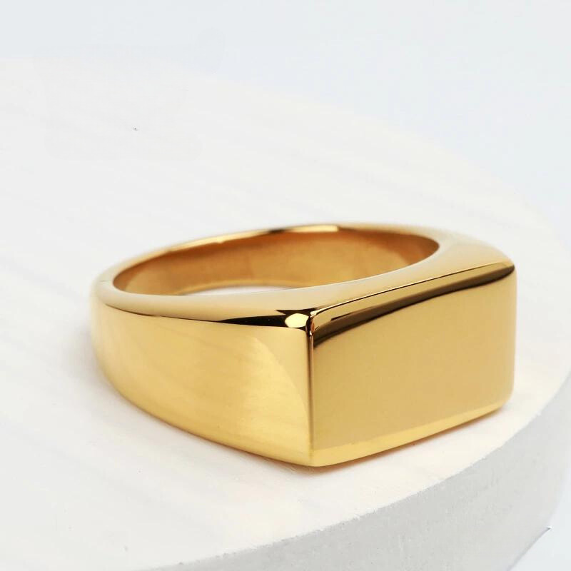Anel masculino Flat Clássico em aço inoxidável dourado colocado sobre uma superfície clara, destacando seu design minimalista.