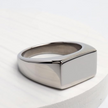 Anel masculino Flat Clássico em aço inoxidável prata colocado sobre uma superfície clara, destacando seu design minimalista.