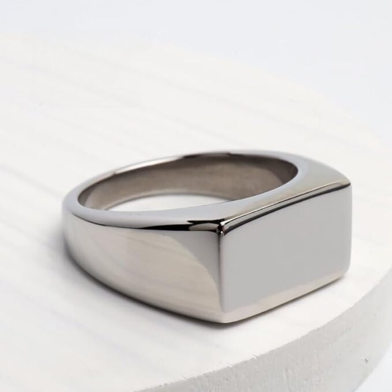 Anel masculino Flat Clássico em aço inoxidável prata colocado sobre uma superfície clara, destacando seu design minimalista.