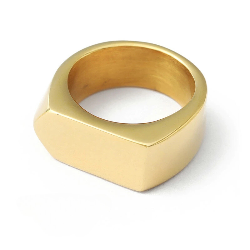 Anel masculino Flat Seta em aço inoxidável dourado deitado sobre fundo branco, destacando seu formato robusto e o detalhe em seta na parte superior.