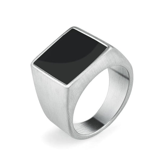 Anel masculino quadrado em aço prata com pedra preta lisa, exibido em fundo claro para destacar o contraste elegante entre a pedra e o metal.
