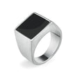 Anel masculino quadrado em aço prata com pedra preta lisa, exibido em fundo claro para destacar o contraste elegante entre a pedra e o metal.