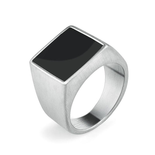 Anel masculino quadrado em aço prata com pedra preta lisa, exibido em fundo claro para destacar o contraste elegante entre a pedra e o metal.