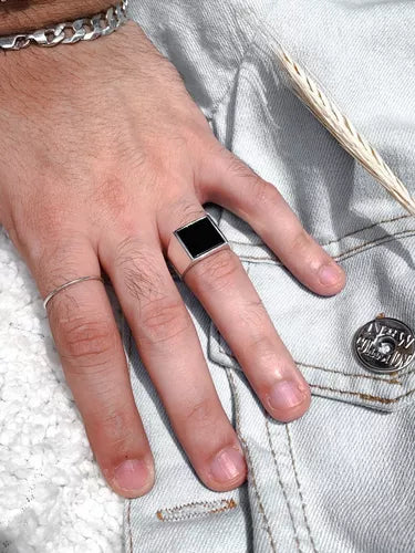 Anel masculino quadrado em aço prata com pedra preta lisa, sendo usado no dedo para mostrar seu ajuste e design imponente