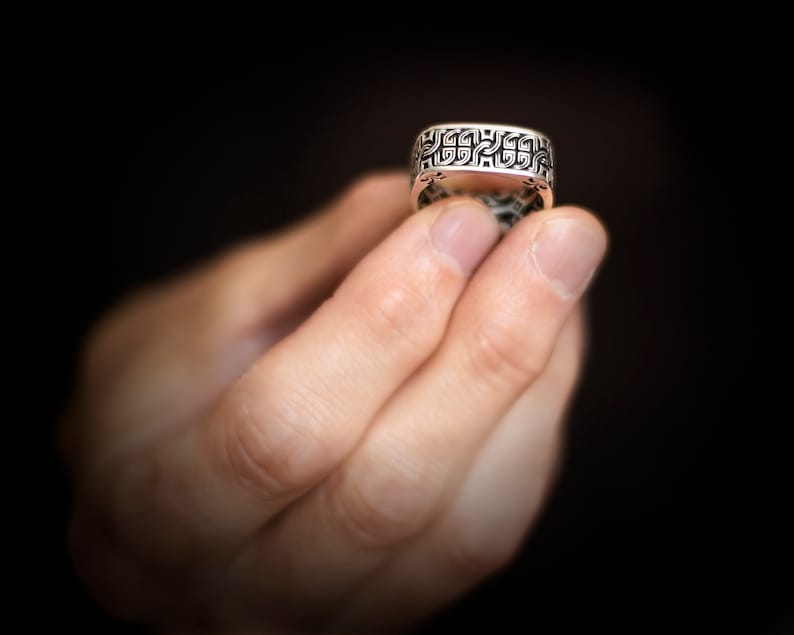 Pessoa segurando o anel masculino retro quadrado na ponta dos dedos, exibindo detalhes do acabamento e estilo.