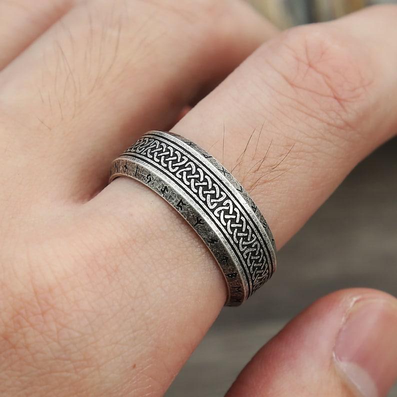  Anel masculino Guerreiro Viking em aço na cor prata antiga, sendo usado no dedo de uma pessoa, destacando o design detalhado e a cor envelhecida.
