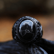 Anel masculino Inca Black em aço inoxidável com pedra texturizada, capturado de um segundo ângulo em fundo preto, enfatizando o contraste entre a pedra e o metal.