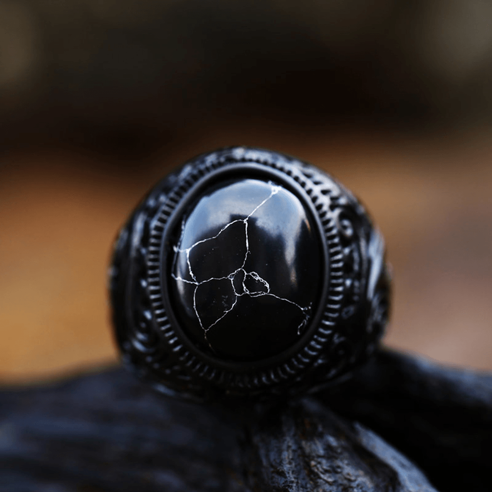 Anel masculino Inca Black em aço inoxidável com pedra texturizada, capturado de um segundo ângulo em fundo preto, enfatizando o contraste entre a pedra e o metal.
