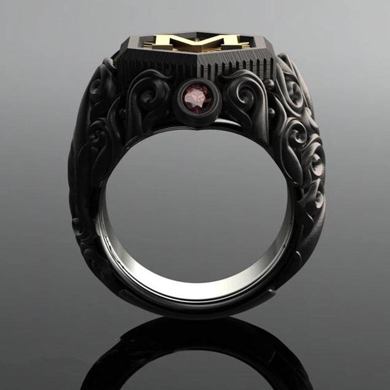 Anel masculino preto maçônico esculpido, mostrado de um terceiro ângulo em fundo cinza escuro, enfatizando os detalhes da joia.