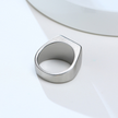 Anel masculino quadrado em aço prata com pedra preta lisa, mostrado de um ângulo diferente em fundo claro para capturar os detalhes do design