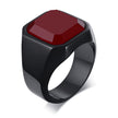 Anel masculino quadrado com pedra vermelha em aço preto, exibido em fundo branco para destacar o contraste entre a pedra e o anel