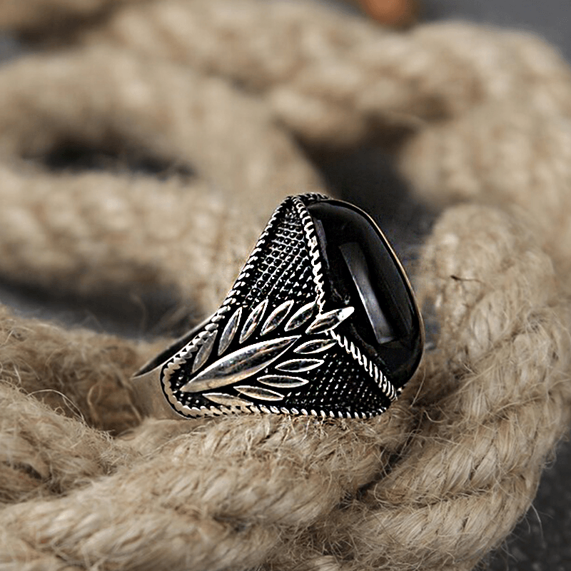 Anel masculino turco com pedra ônix preta, capturado de um ângulo lateral em um fundo de corda, destacando os detalhes rústicos do design.