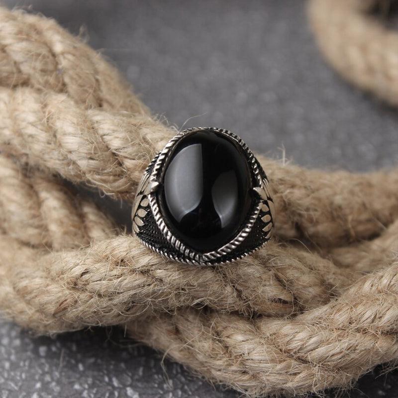 Anel masculino turco com pedra ônix preta, exibido de um segundo ângulo sobre um fundo de corda, realçando a pedra e os detalhes da prata.