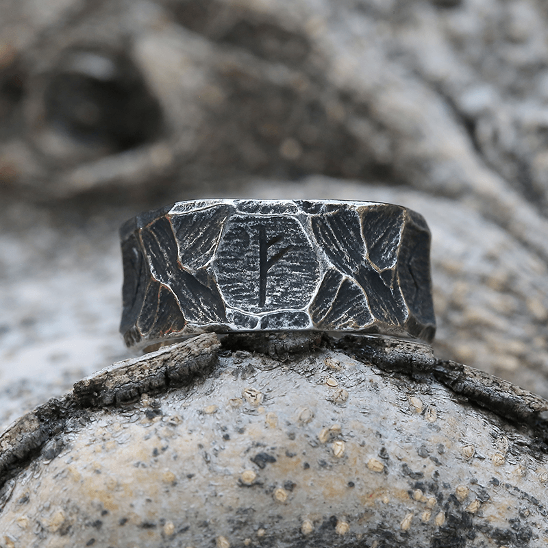 Anel masculino Viking rústico em aço prata, exibido sobre um fundo rochoso claro para destacar seu design robusto e sua inspiração viking.