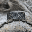Anel masculino Viking rústico em aço prata, exibido sobre um fundo rochoso claro para destacar seu design robusto e sua inspiração viking.