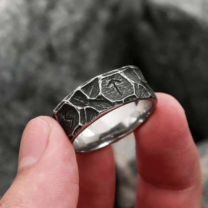Anel masculino Viking rústico em aço prata, segurado na ponta dos dedos para destacar seus detalhes e o acabamento rústico em um ângulo específico.