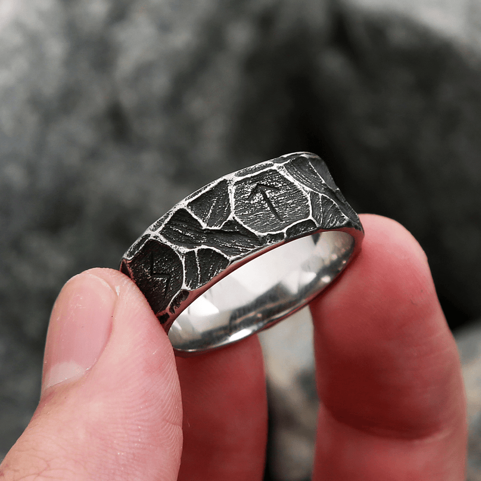 Anel masculino Viking rústico em aço prata, segurado na ponta dos dedos para destacar seus detalhes e o acabamento rústico em um ângulo específico.