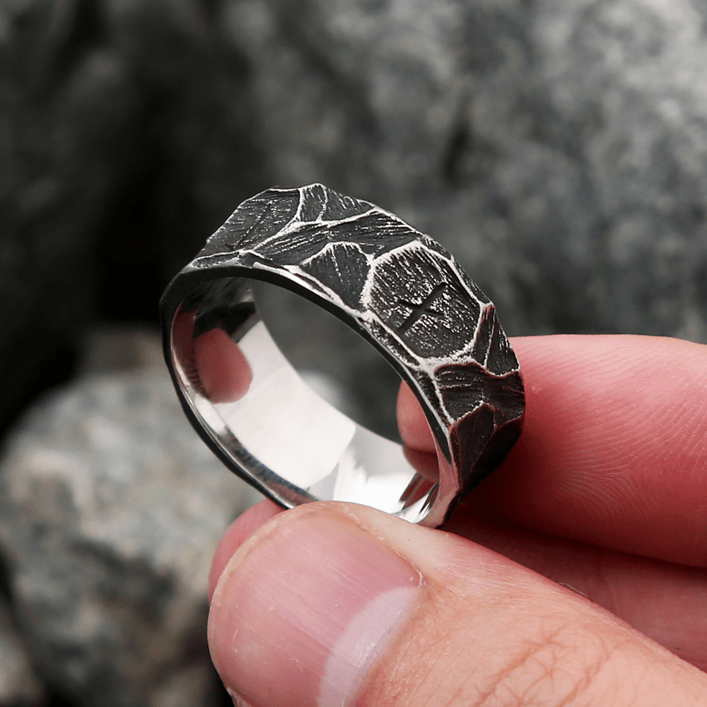 Anel masculino Viking rústico em aço prata, mostrado de outro ângulo enquanto é segurado na ponta dos dedos, evidenciando sua textura e estilo