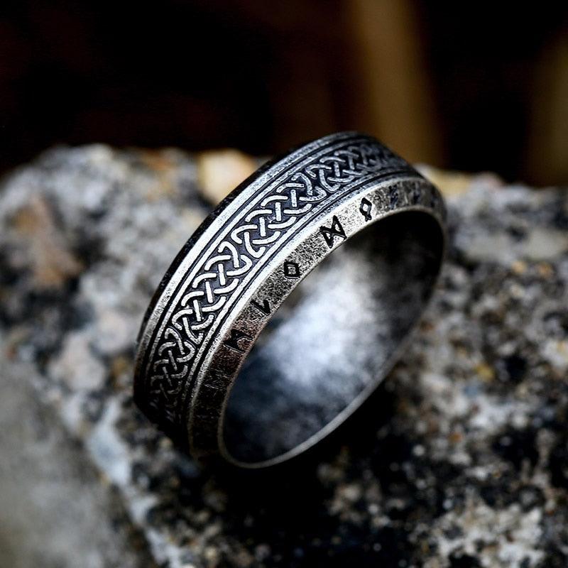Anel masculino Guerreiro Viking em aço na cor prata antiga, exibido sobre um fundo rochoso cinza, destacando os detalhes e a cor envelhecida do anel.